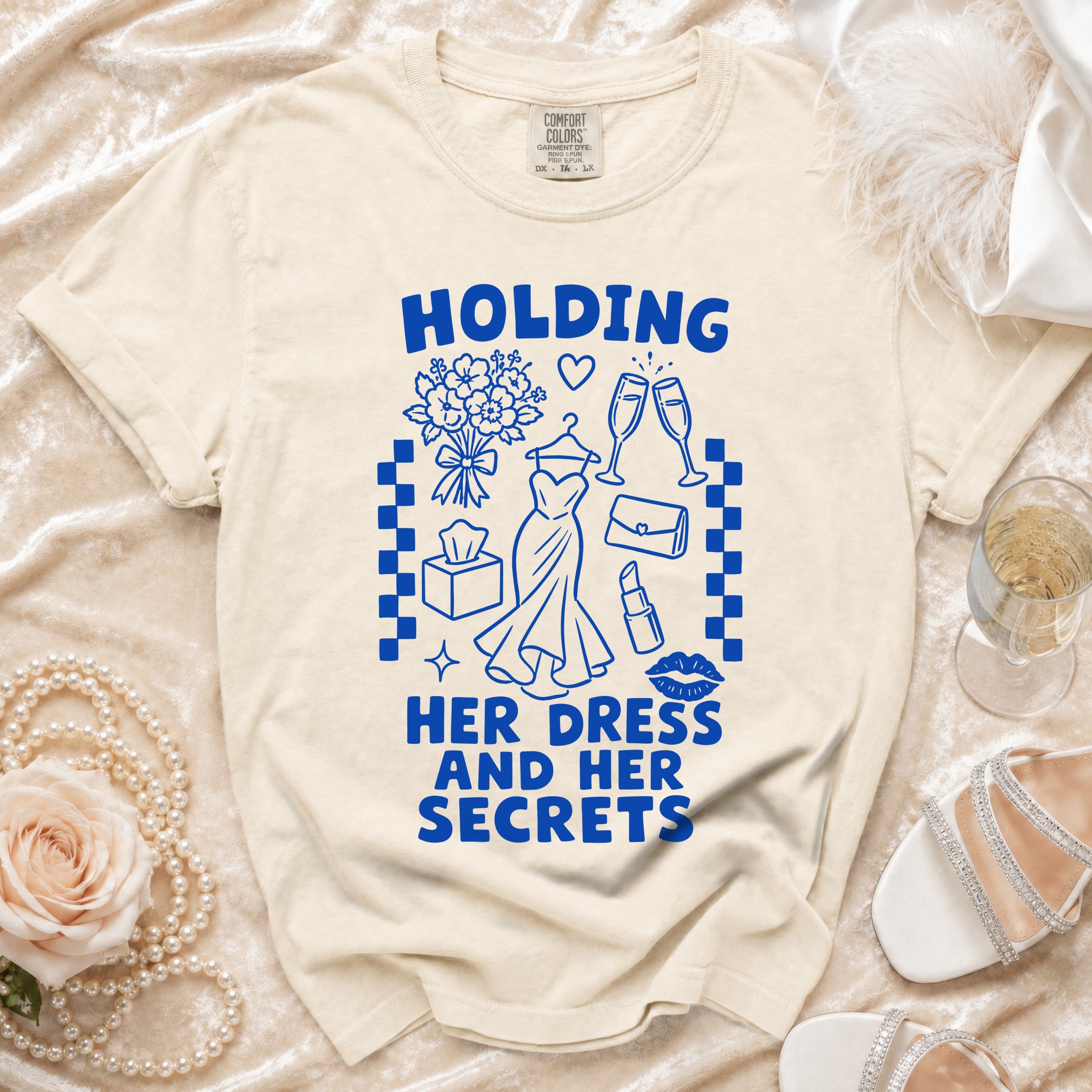 Ecru t-shirt with blue text "HOLDING HER DRESS AND HER SECRETS" and graphics.
