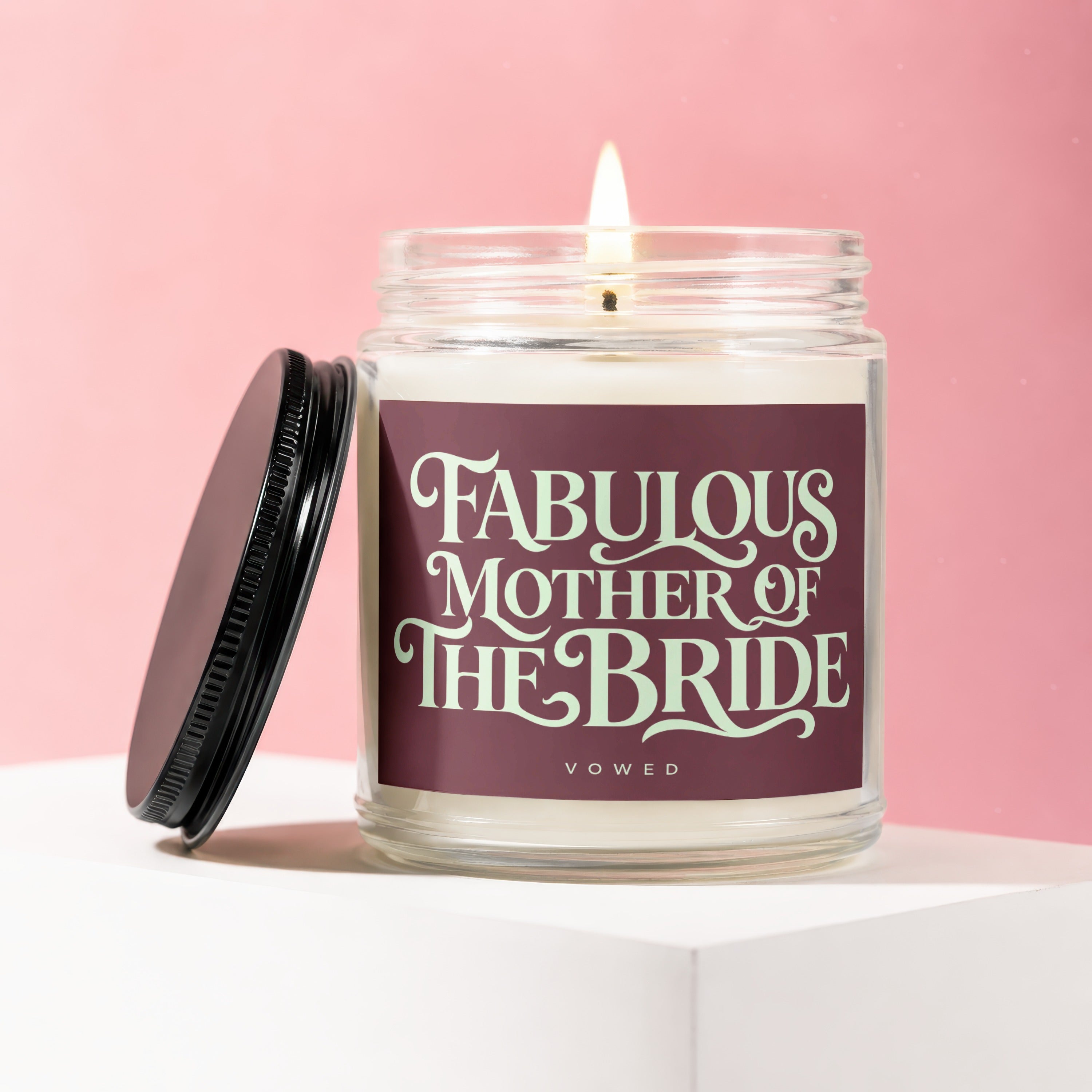 Glass candle with lit wick, burgundy label reading "Fabulous Mother of The Bride".
