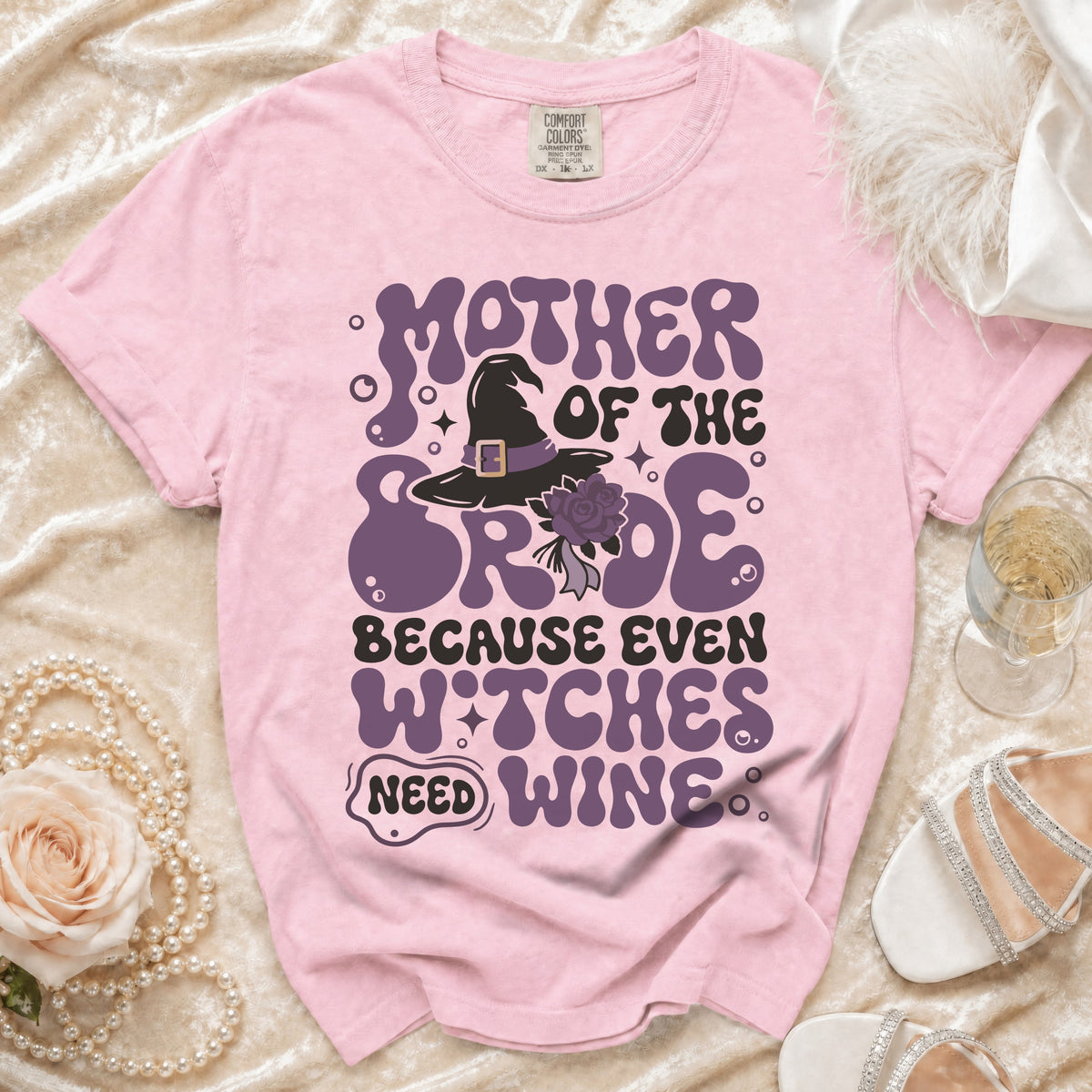 Pink t-shirt with "Mother of the Bride because even witches need wine" text and graphics.