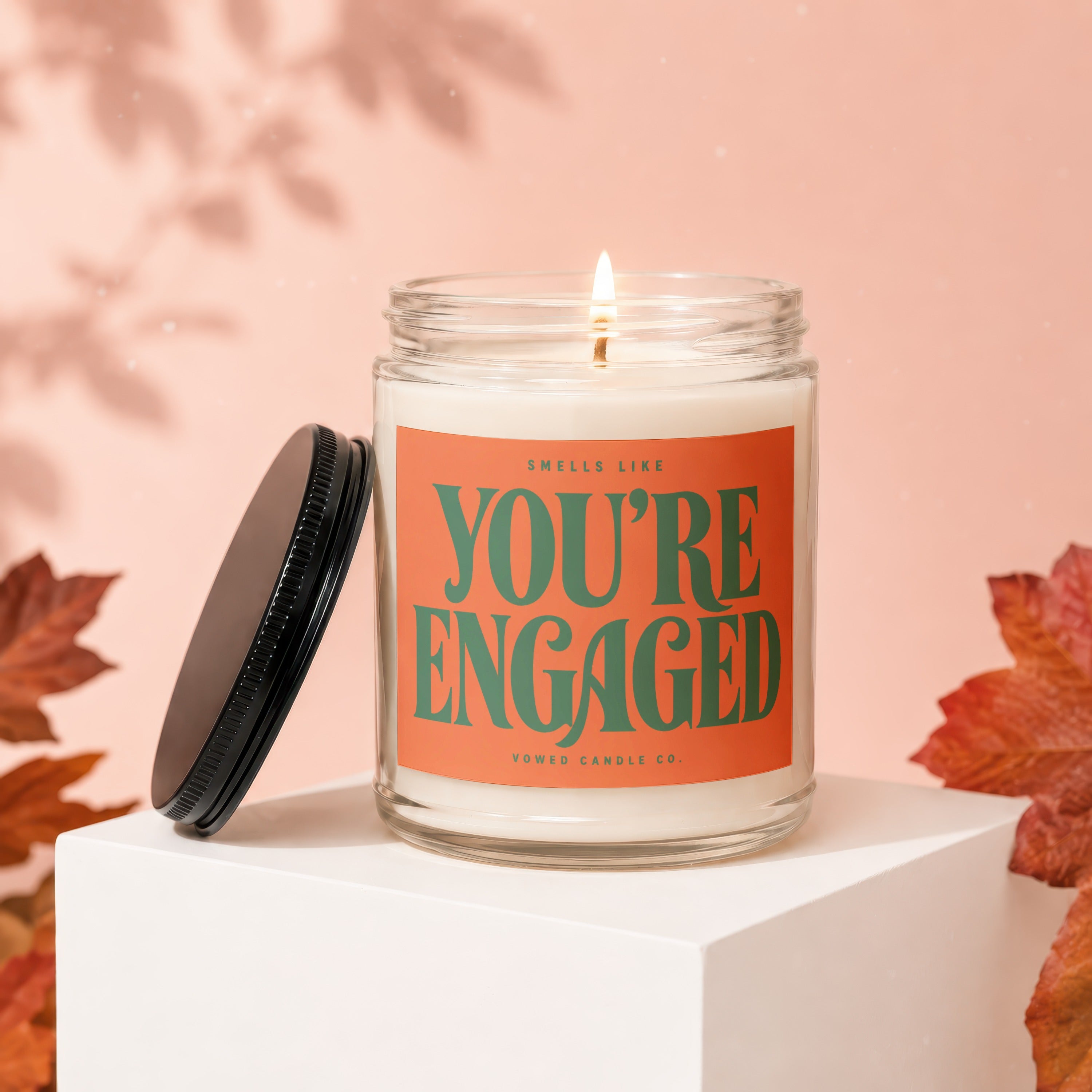 Candle with "You're Engaged" label and lid nearby on pedestal.