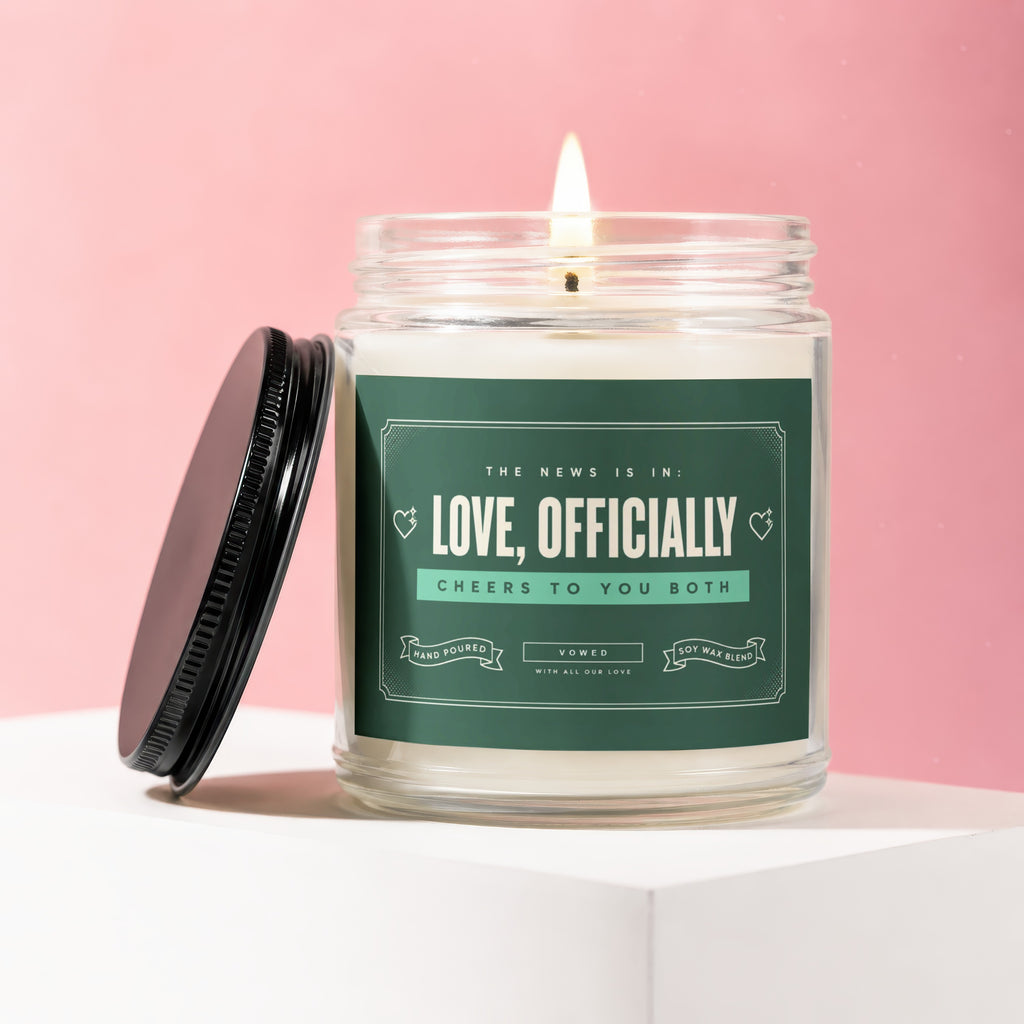 Glass candle with burning wick, label reads "Love, Officially" and "Cheers to you both."