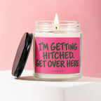 Glass candle with lit wick and black lid. Pink label reads "I'M GETTING HITCHED. GET OVER HERE."
