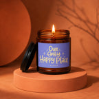Lit amber glass candle with label that reads "Our Only Happy Place"