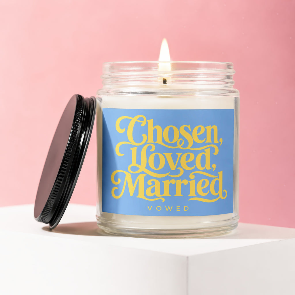 Scented candle with text "Chosen, Loved, Married, Vowed" on a blue label.
