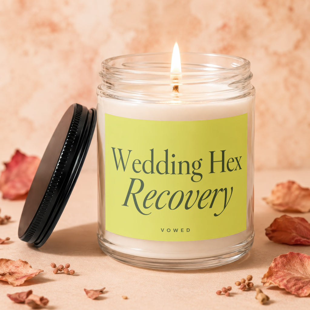 Glass candle with lit wick, yellow label reading "Wedding Hex Recovery VOWED."