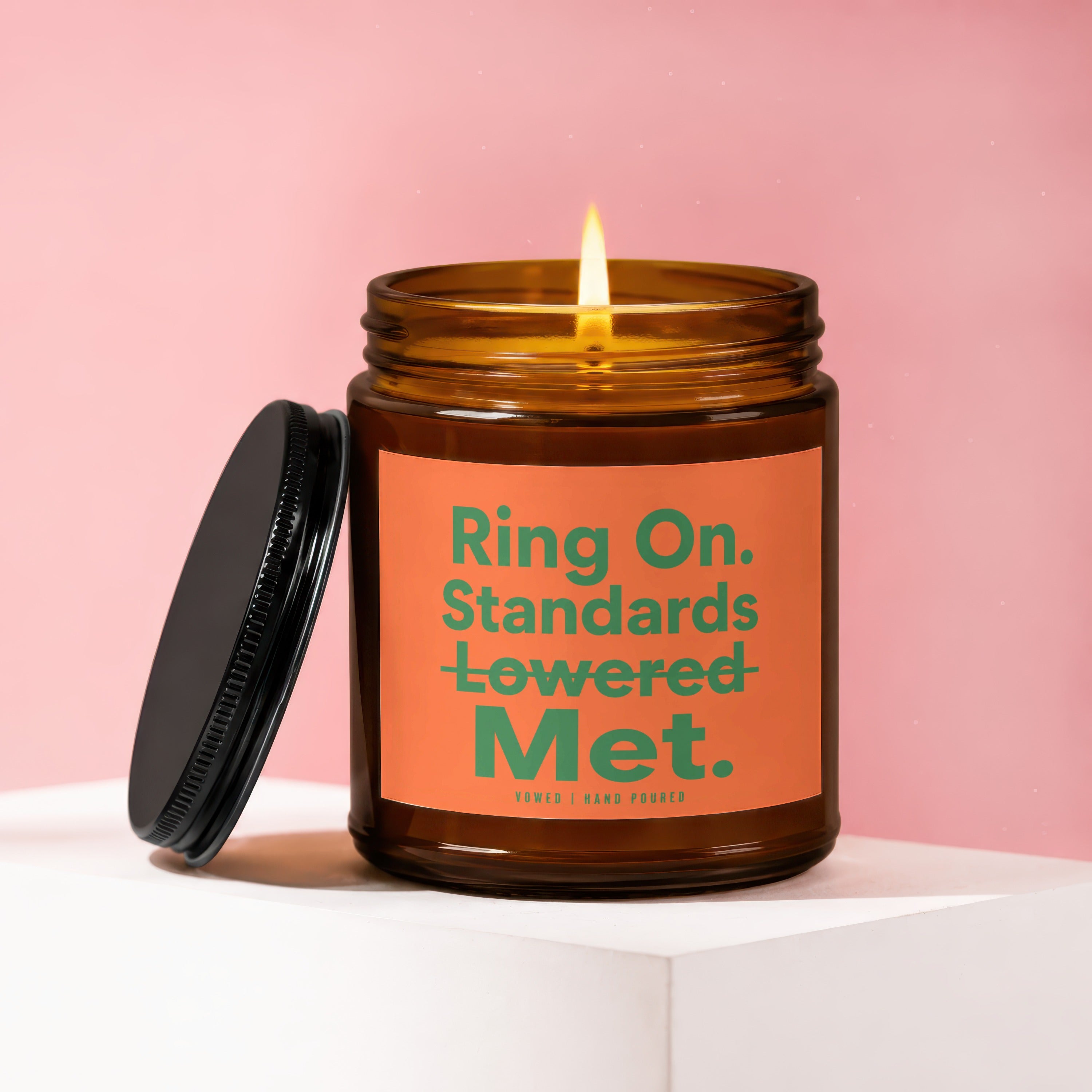 Amber jar candle with lit flame and black lid, reads "Ring On. Standards Lowered Met."