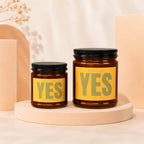 Two amber glass candles with black lids and yellow labels reading "Smells Like Yes".