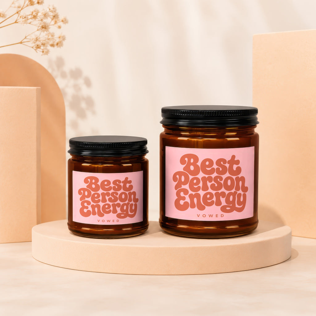 Two amber glass candles with "Best Person Energy" labels are displayed on peach pedestals.