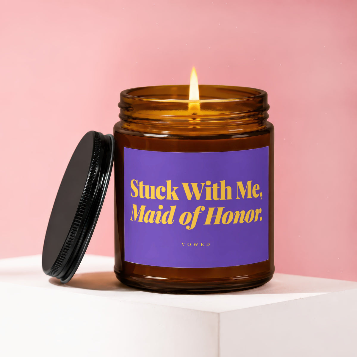 Brown glass candle with lit flame and purple label saying "Stuck With Me, Maid of Honor."