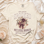 Cream t-shirt with "Spooked but still booked" text, pumpkin, and flowers design.