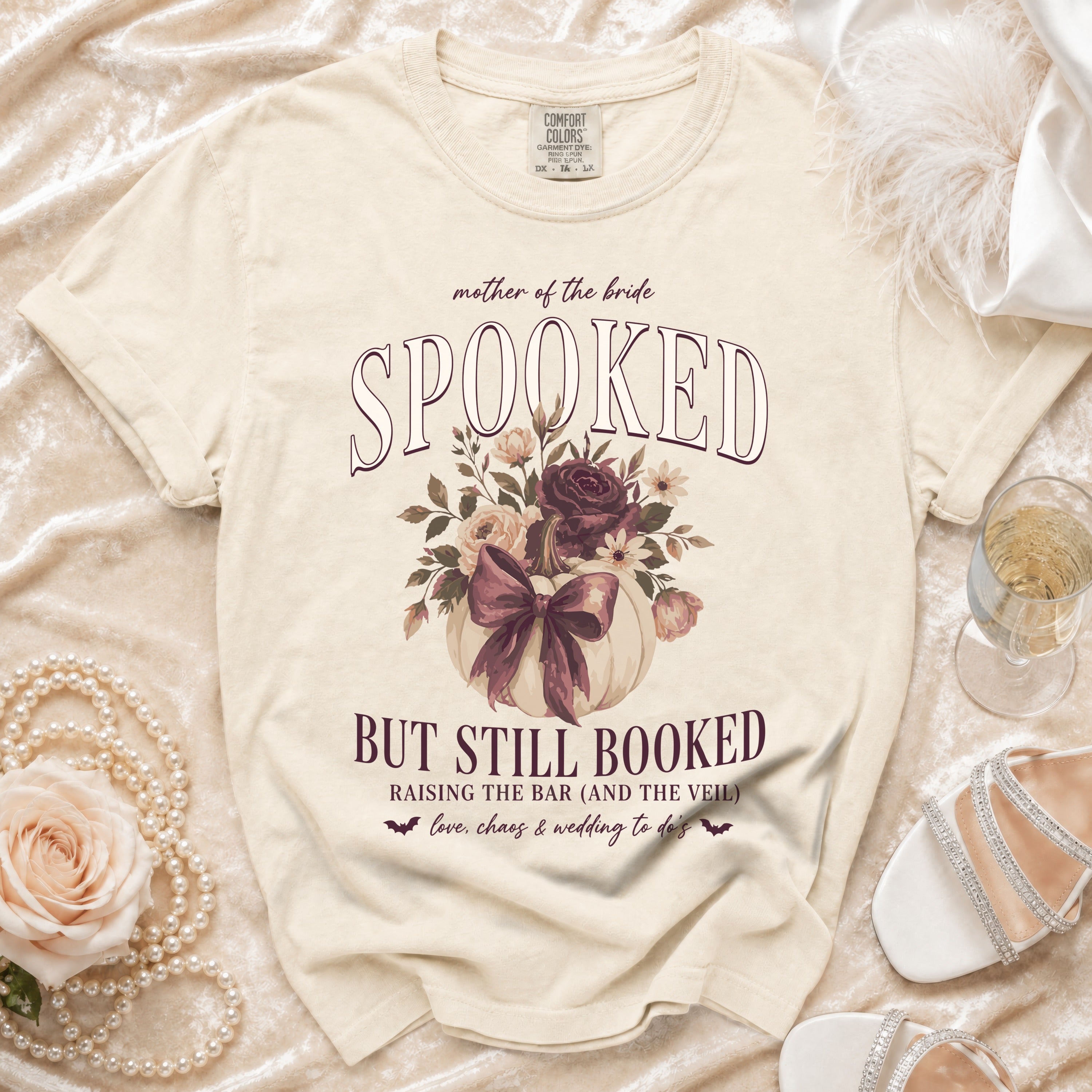 Cream t-shirt with "Spooked but still booked" text, pumpkin, and flowers design.