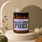 Candle labeled "Maid of Honor Fuel Apply Liberally Vowed" on display pedestal.