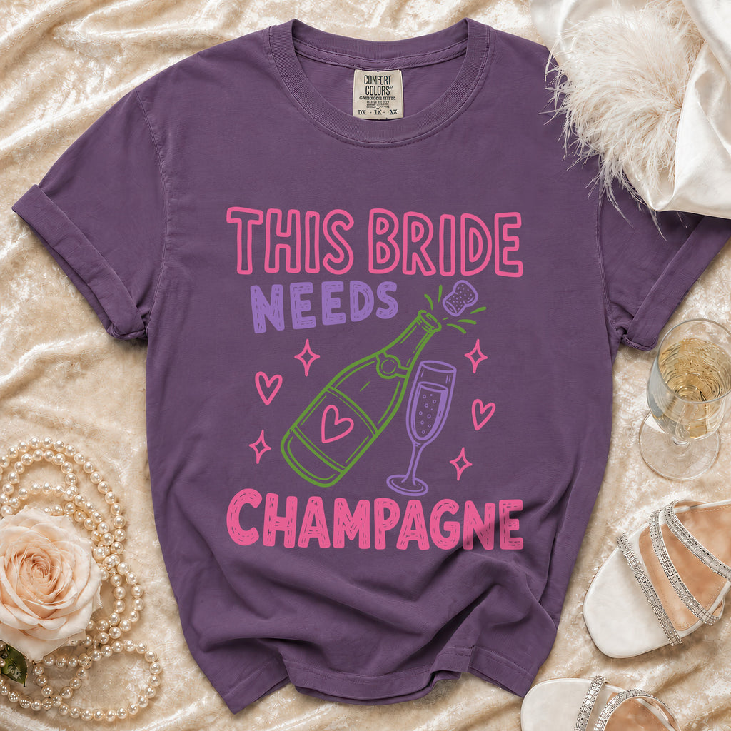 Purple t-shirt with "This Bride Needs Champagne" text and champagne bottle graphic.