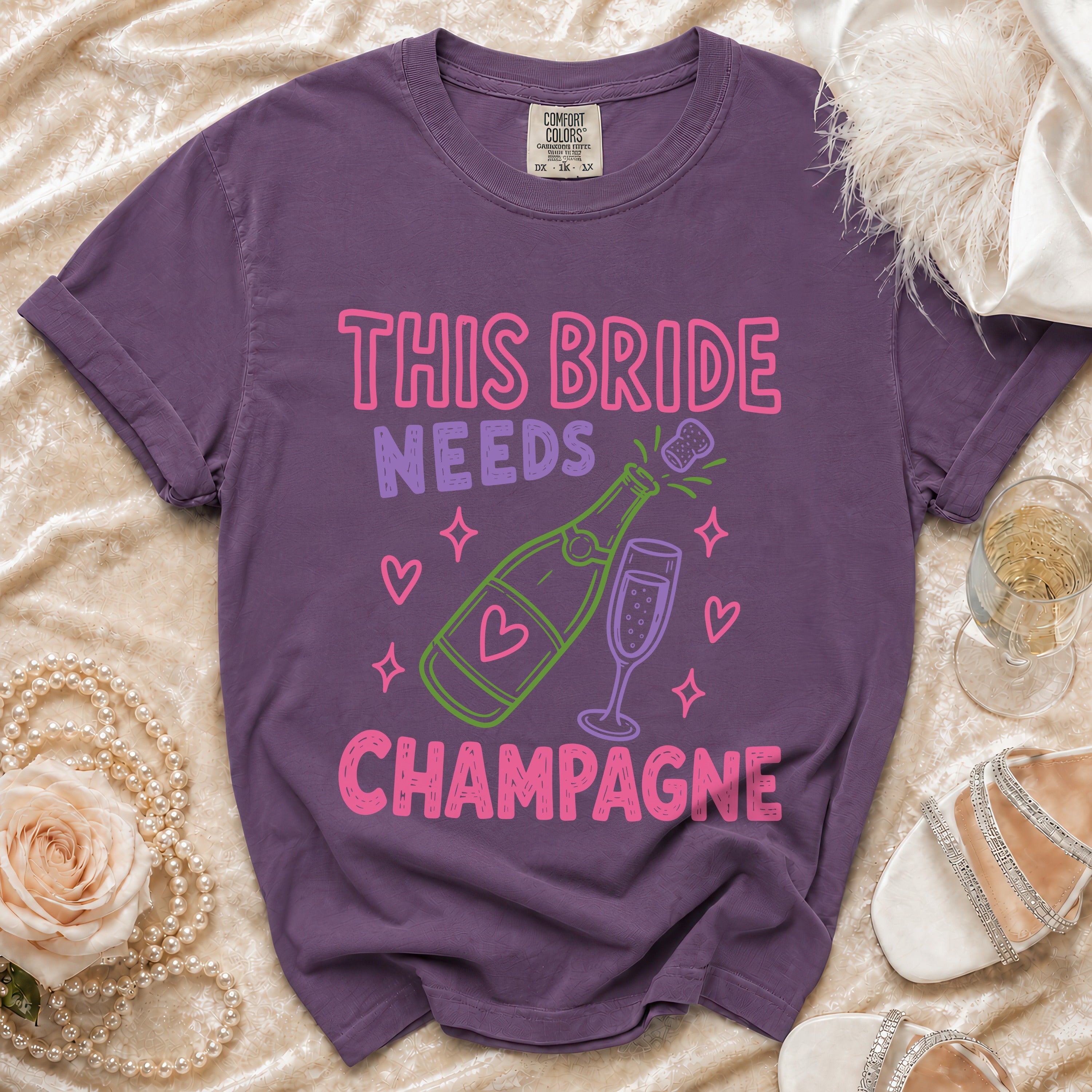 Purple t-shirt with "This Bride Needs Champagne" text and champagne bottle graphic.