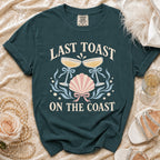 Teal t-shirt with "Last Toast On The Coast" text and nautical graphics.