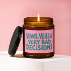 Amber candle with lit flame and pink label reading "Vows, Veils & Very Bad Decisions".