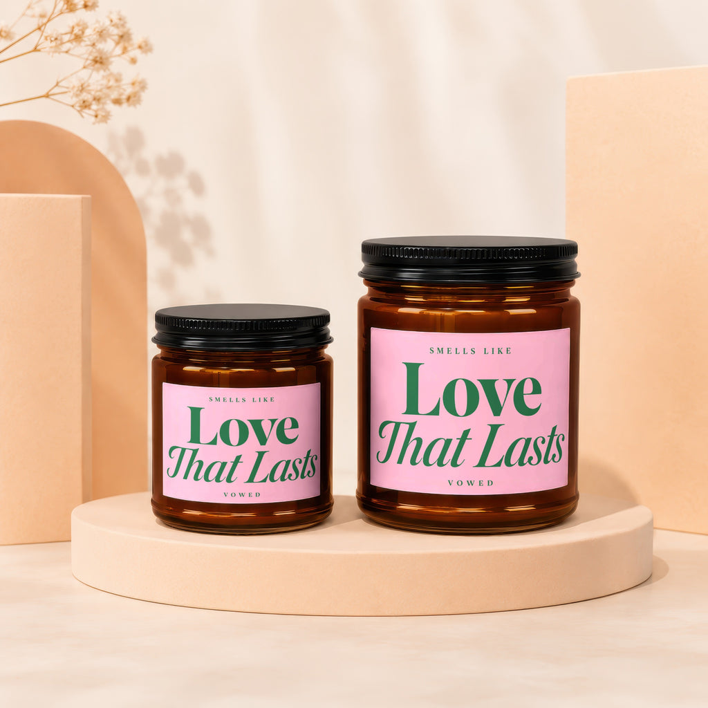 Two amber glass candles with pink labels reading "Smells Like Love That Lasts".