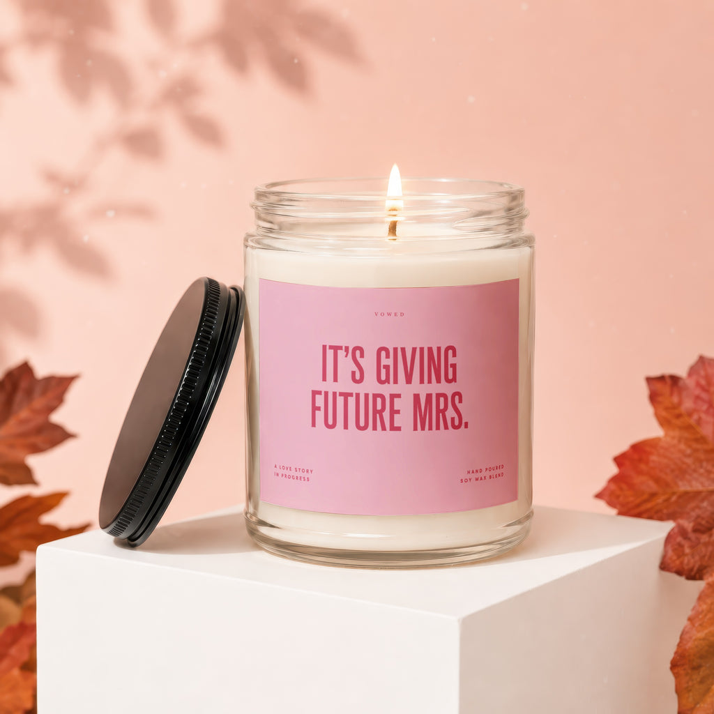 Glass jar candle with pink label reading "IT'S GIVING FUTURE MRS."