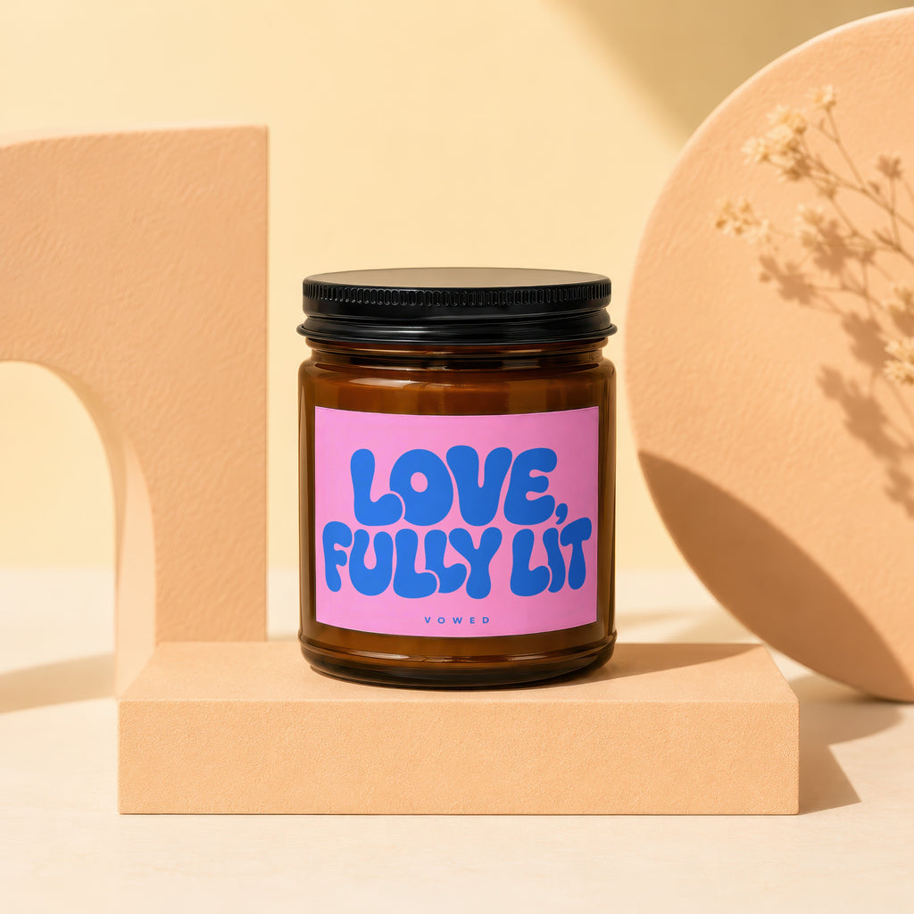 Brown glass candle with pink label saying "LOVE, FULLY LIT" by VOWED.