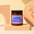 Brown glass candle with pink label saying "LOVE, FULLY LIT" by VOWED.