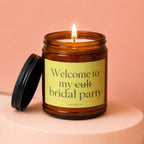 Amber jar candle with lit wick and black lid, label reads "Welcome to my cult bridal party VOWED".