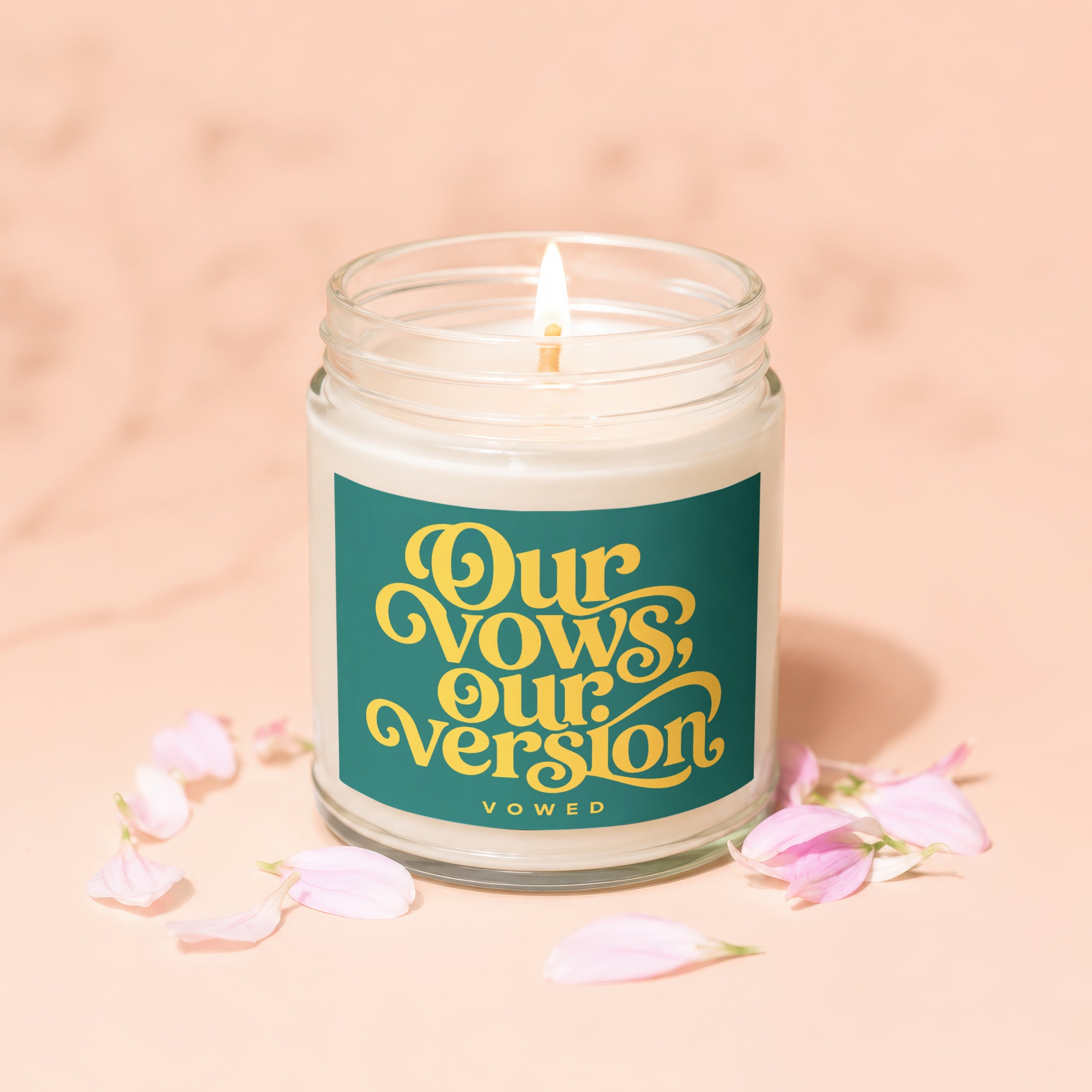 Burning candle in glass jar with "Our Vows, Our Version" text and flower petals.