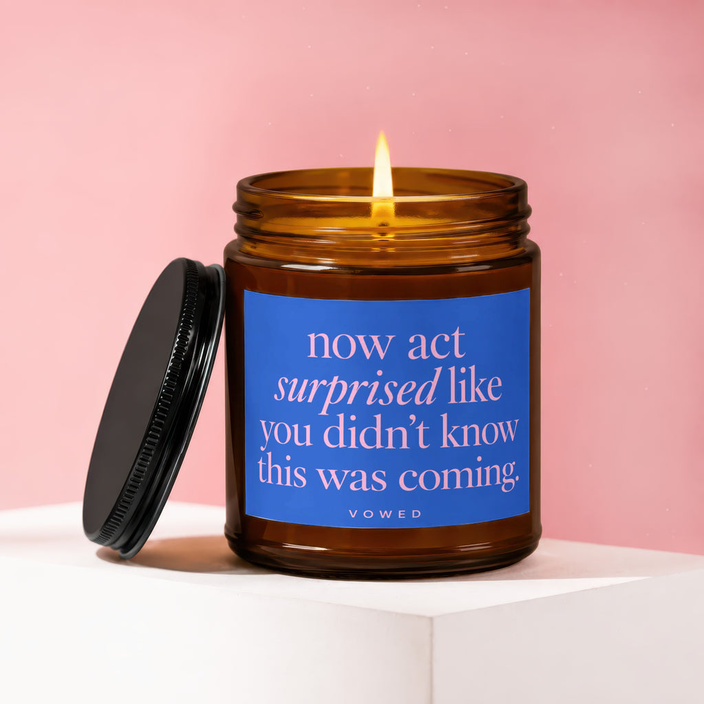 Amber jar candle with blue label saying "now act surprised like you didn't know this was coming. vowed."