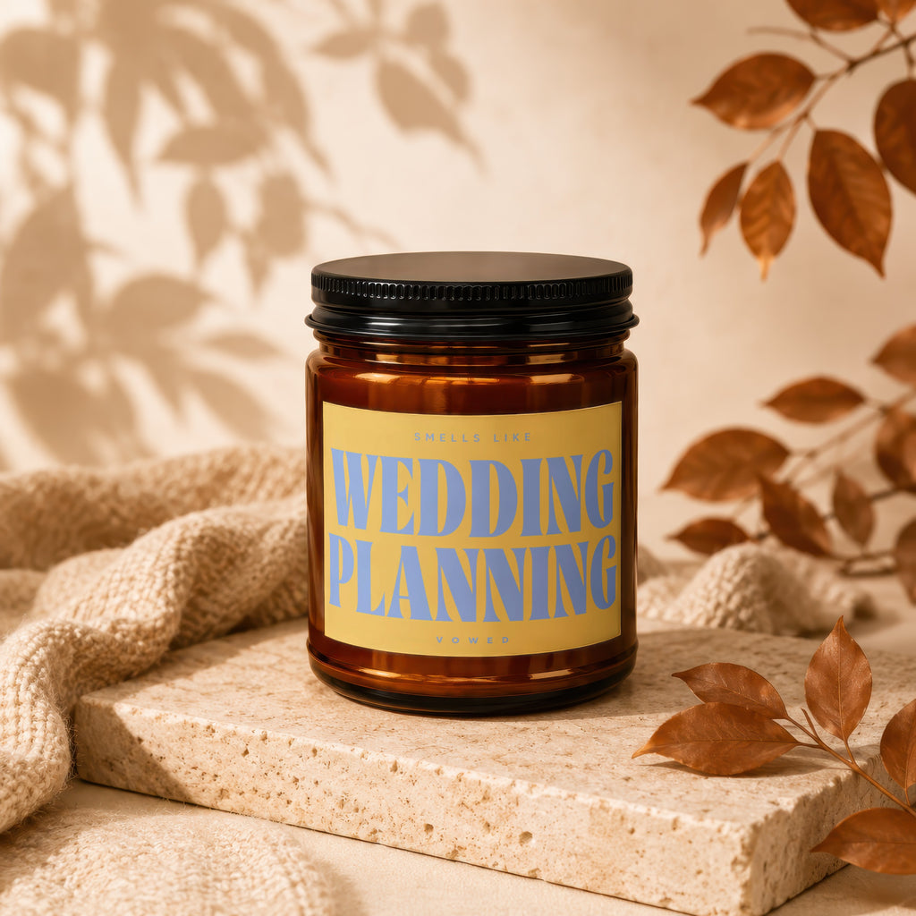 Amber candle with "Wedding Planning" text on a yellow label, surrounded by autumn leaves.