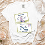 White t-shirt with "Austin, TX Summer 2026 Reckless in Texas Olivia's Bach" text and graphic.