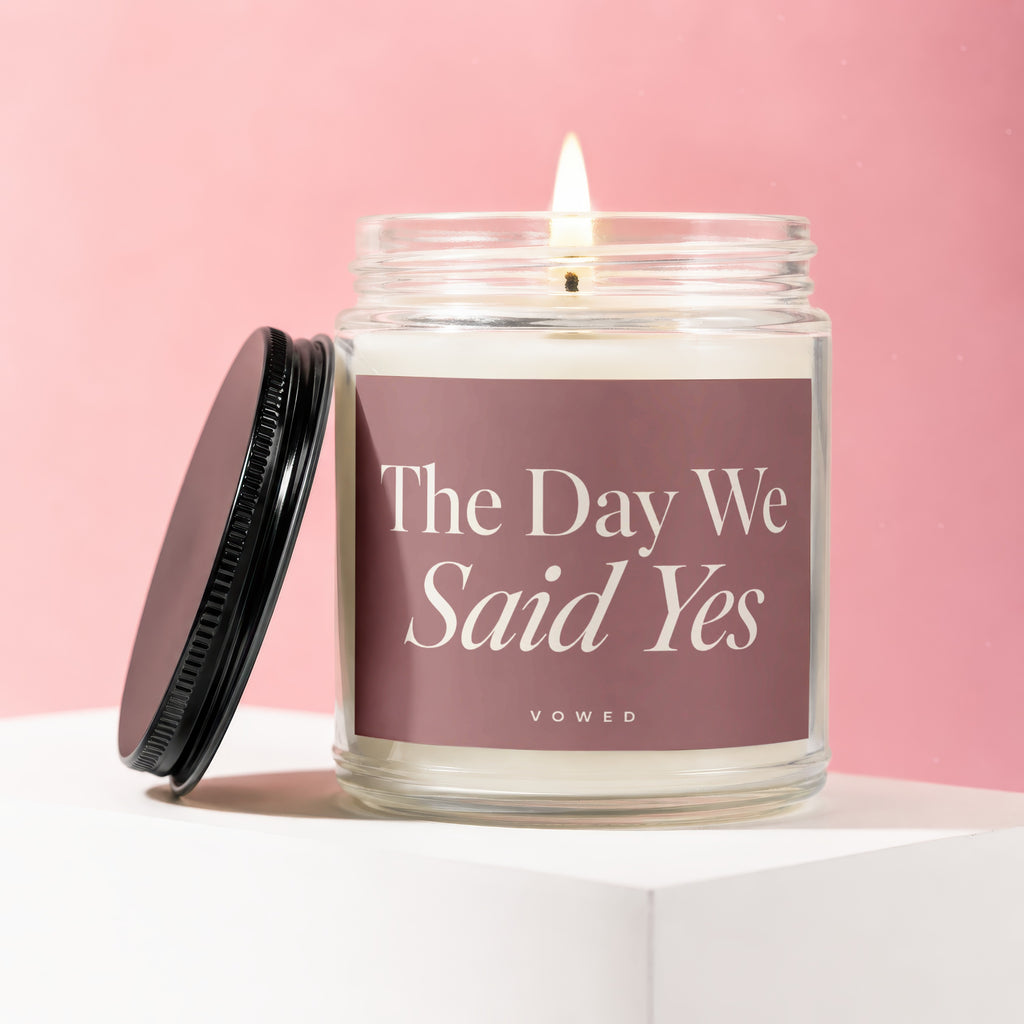 Glass candle with lit wick and lid off, labeled "The Day We Said Yes".