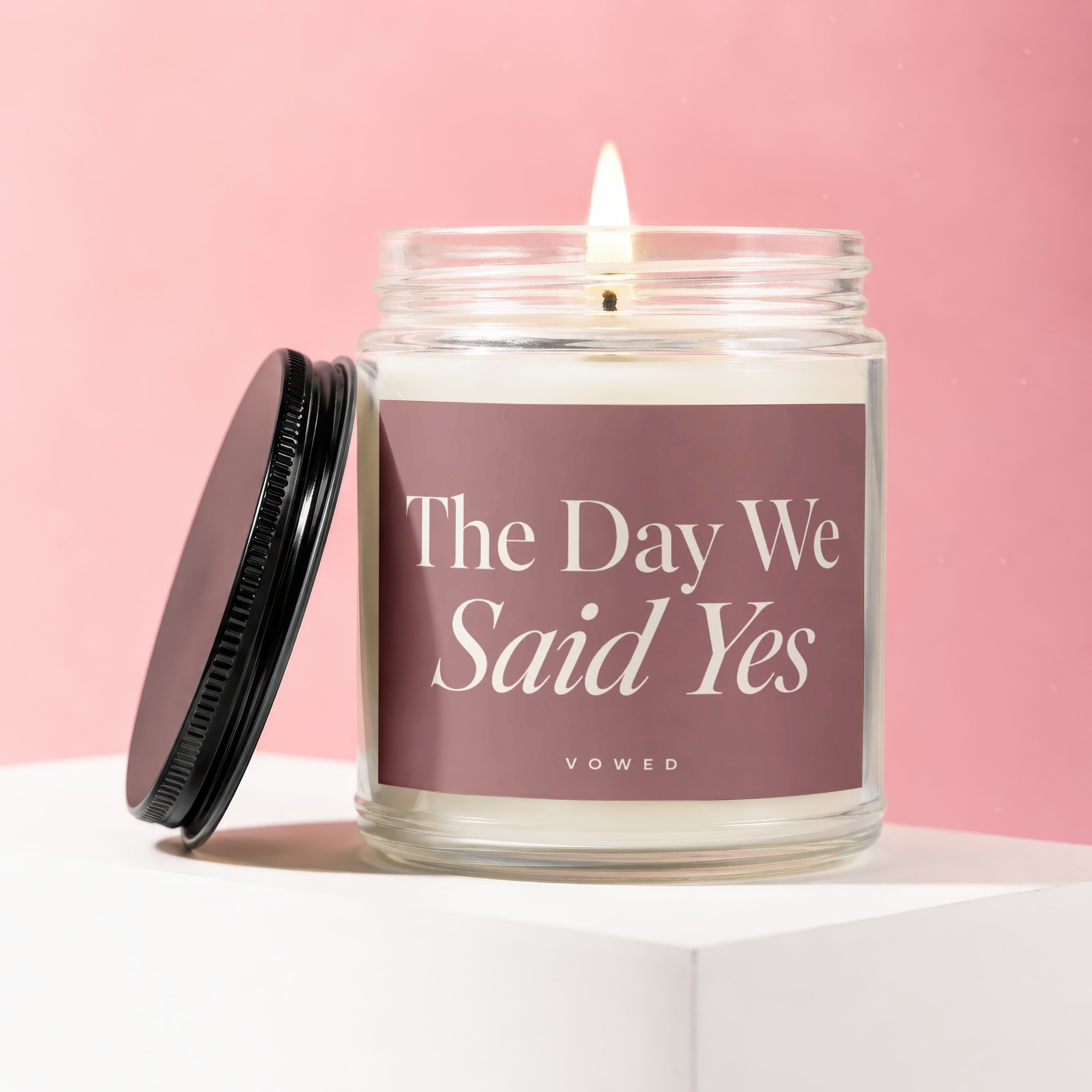 Glass candle with lit wick and lid off, labeled "The Day We Said Yes".