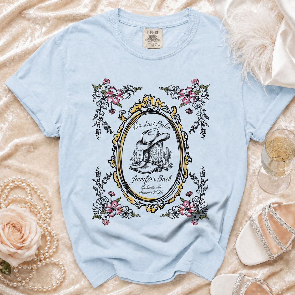 Light blue t-shirt with cowboy boot and floral design and text "Her Last Rodeo".