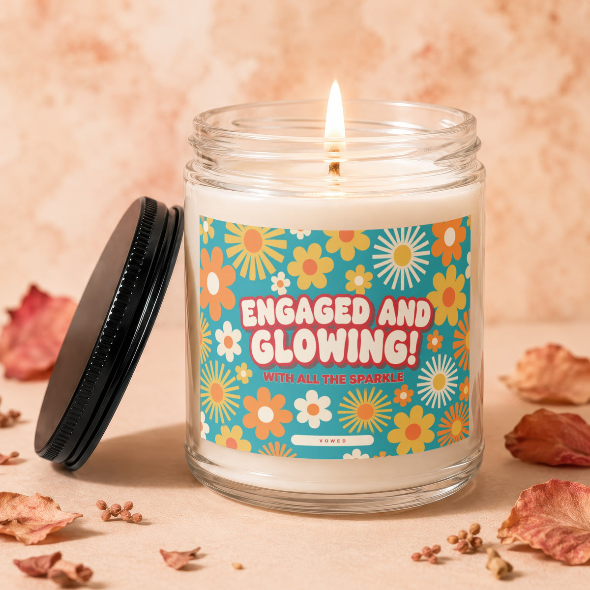 Candle with lid off, flame lit, featuring "ENGAGED AND GLOWING!" text.