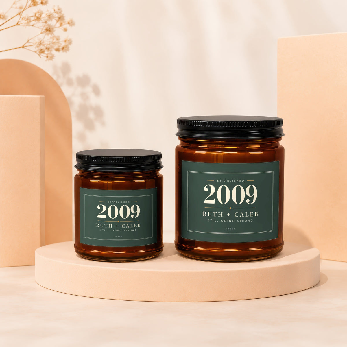 Two amber glass candles with green labels reading "Established 2009 Ruth + Caleb Still Going Strong".