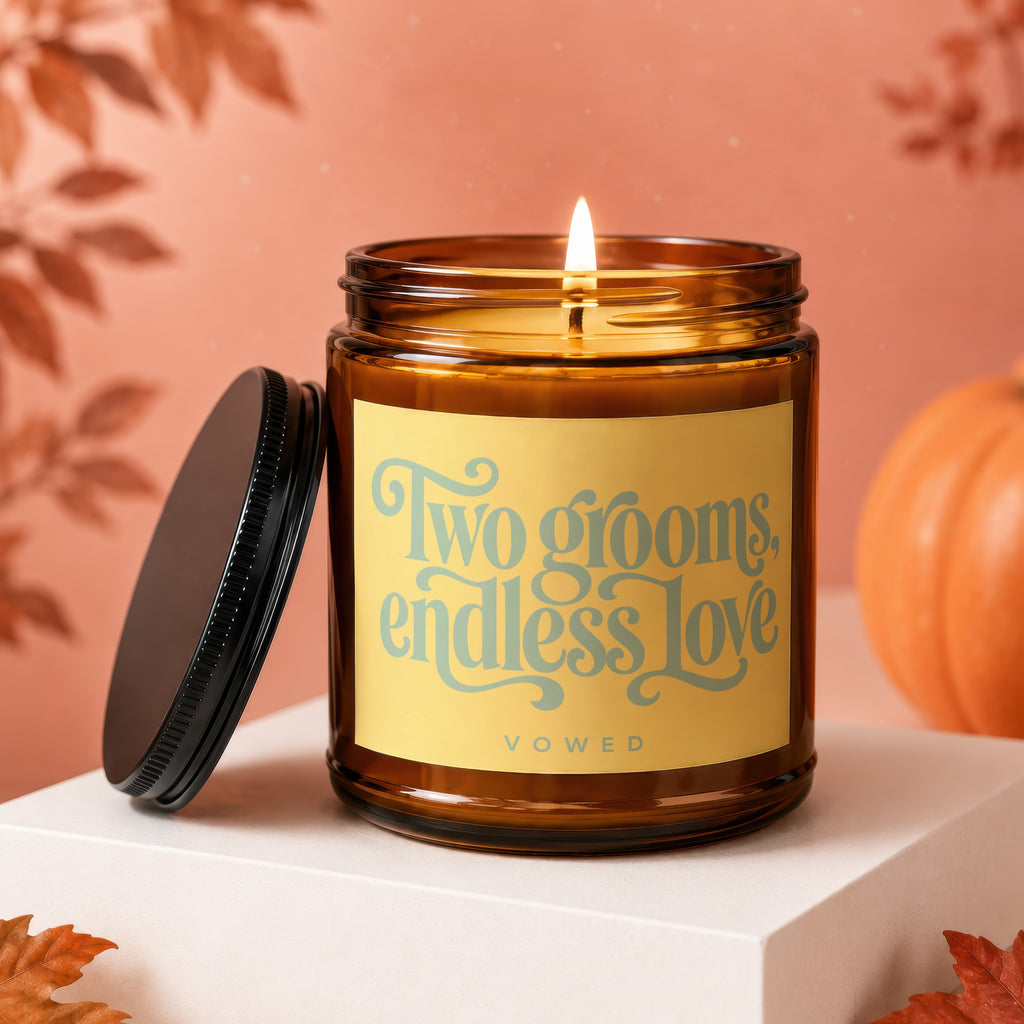 Amber candle with lit wick, "Two grooms, endless love" text, on white cube.