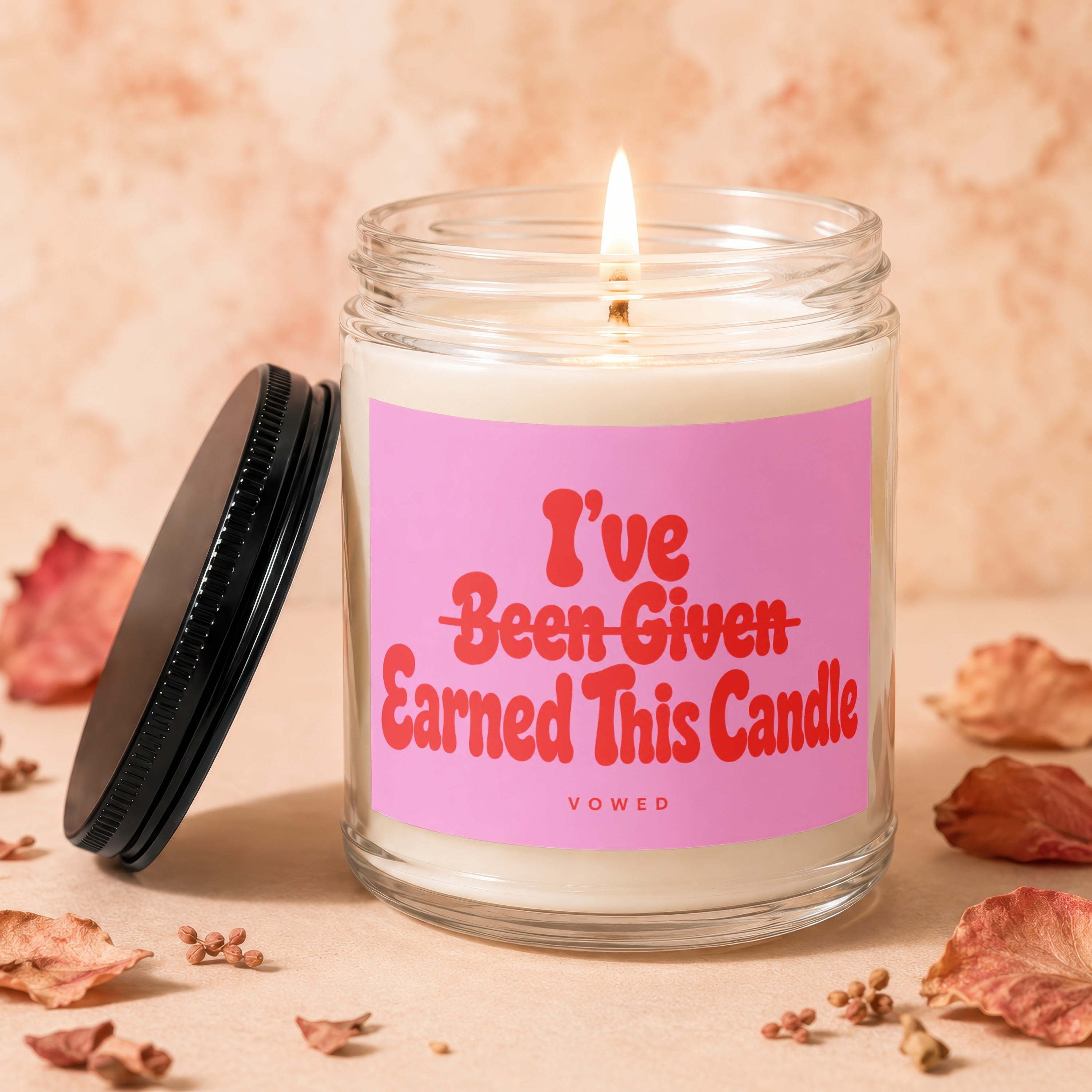 Burning candle in glass jar with pink label reading "I've Earned This Candle"
