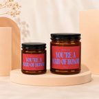 Two amber glass candles with red labels reading "You're a Maid of Honor."