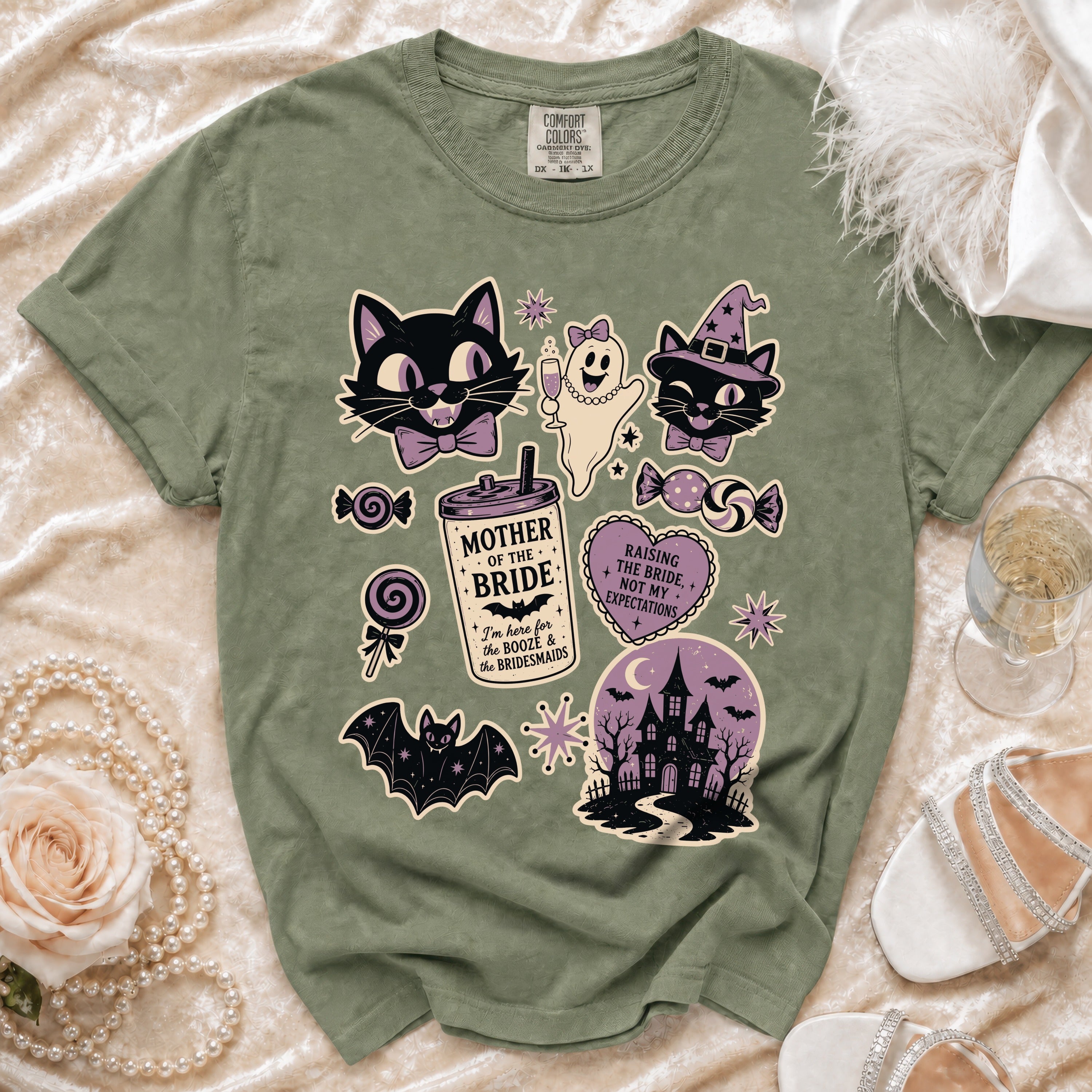 Sage green t-shirt with a vintage Halloween graphic featuring cats, a ghost, a haunted house, and text.
