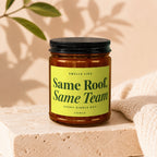 Amber jar candle with black lid, yellow label reads "Smells like Same Roof, Same Team".
