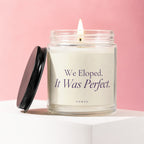 Glass candle with lit flame, cream label reading "We Eloped. It Was Perfect."