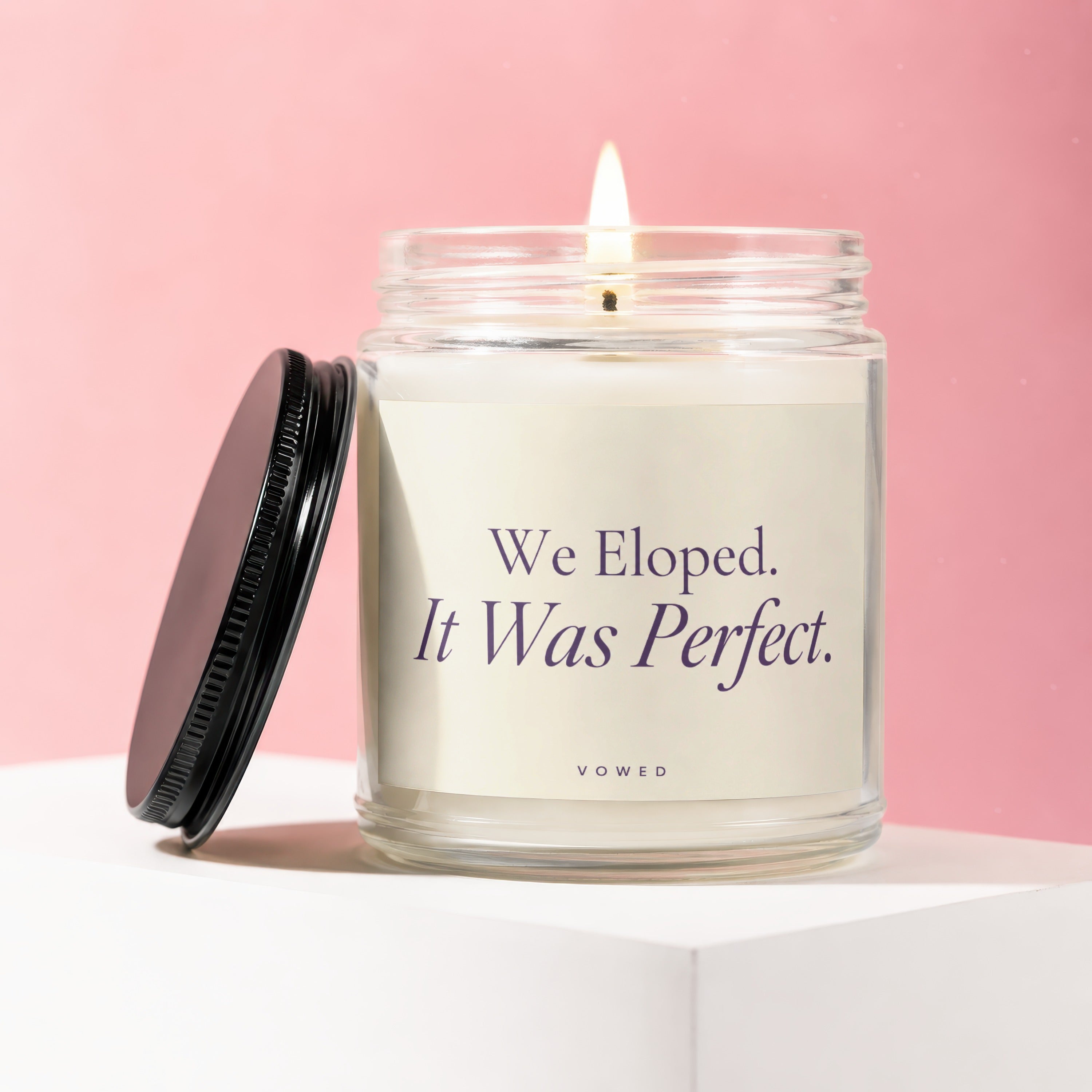 Glass candle with lit flame, cream label reading "We Eloped. It Was Perfect."