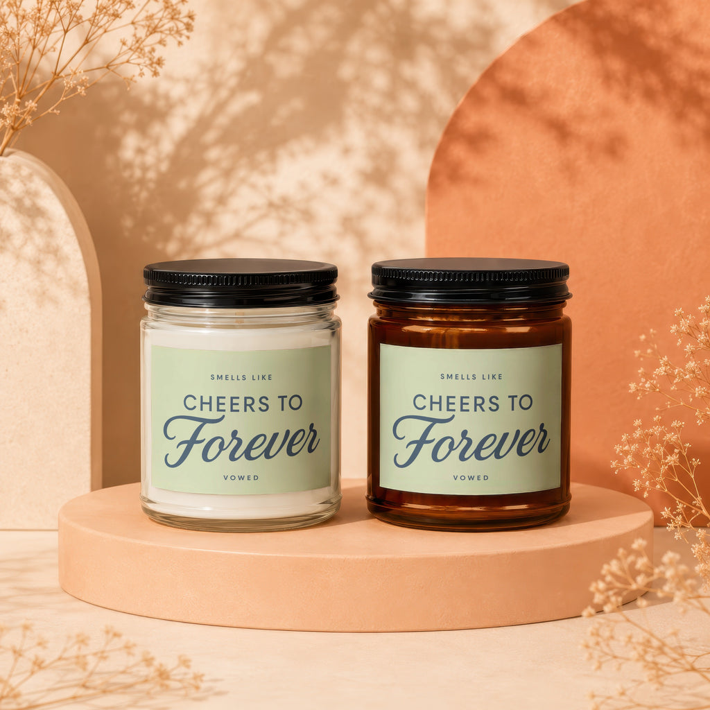Two candles with black lids, labelled "Cheers to Forever," sit on display stands.