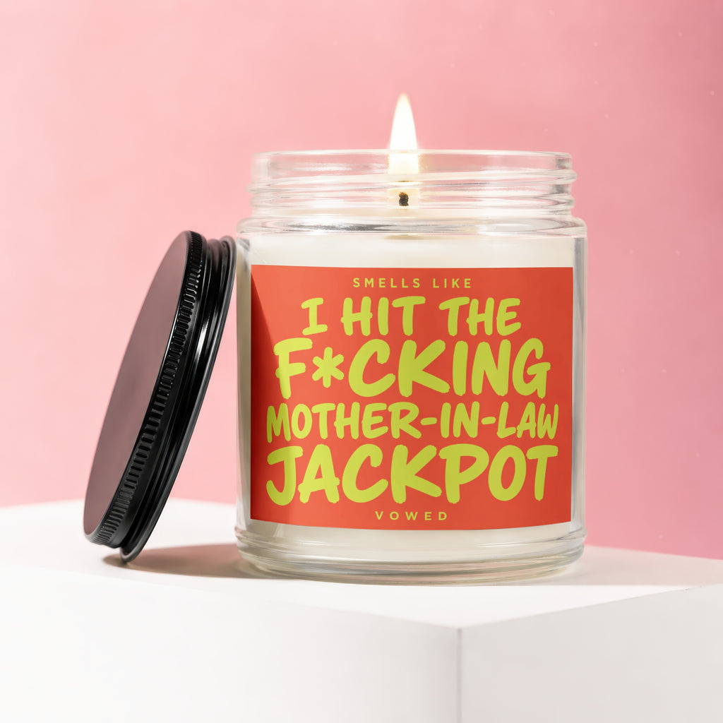 Lit candle in jar with black lid, reads "Smells like I hit the mother-in-law jackpot."