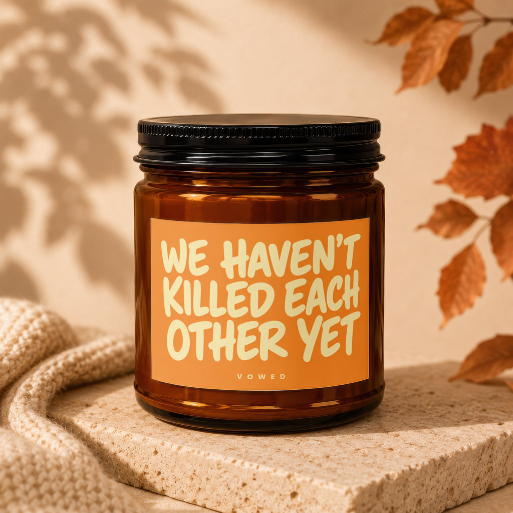 Amber candle with black lid, orange label reading "WE HAVEN'T KILLED EACH OTHER YET".