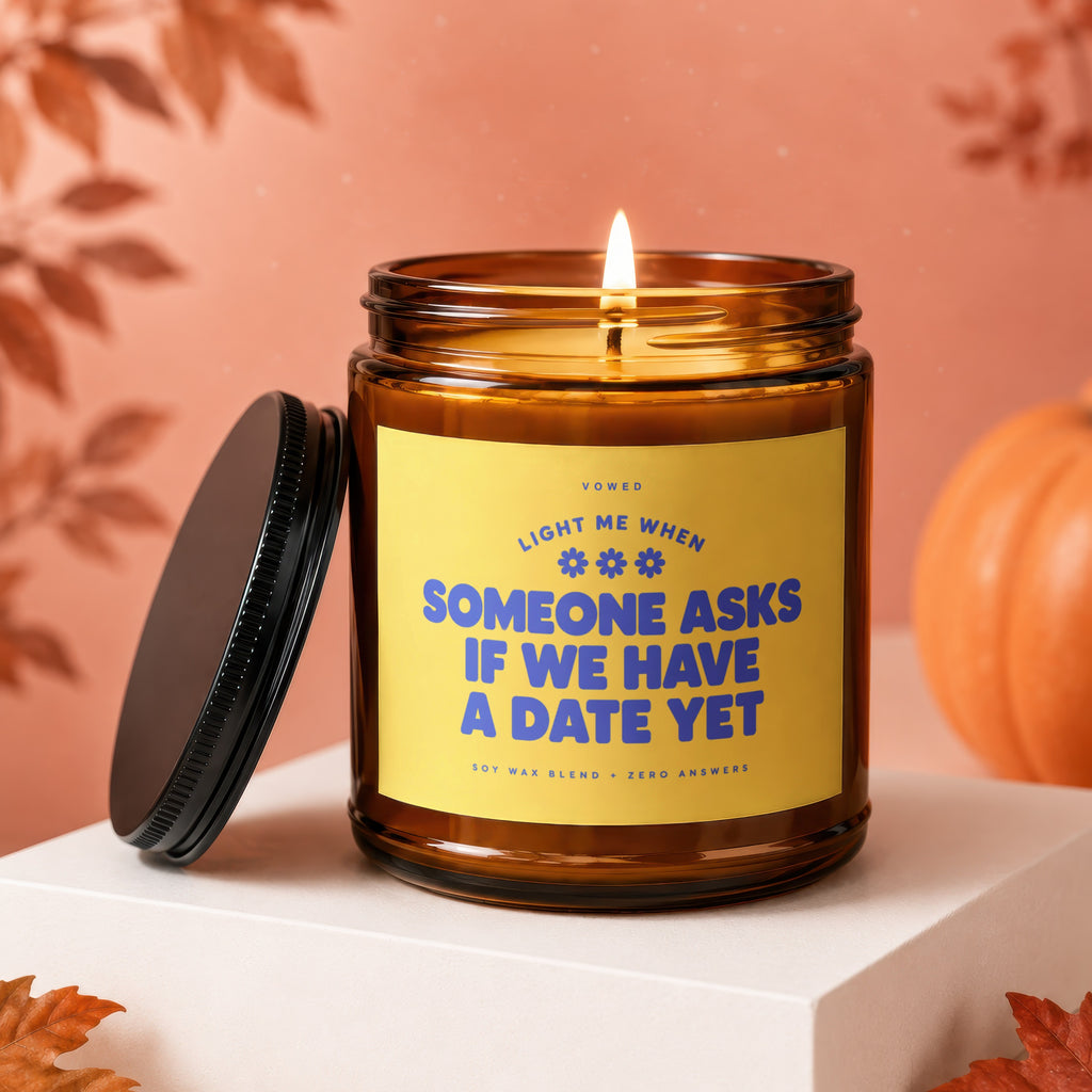 Amber candle with yellow label reading "Light me when someone asks if we have a date yet."