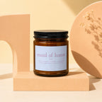 Amber glass candle with "maid of honor" label on beige blocks.