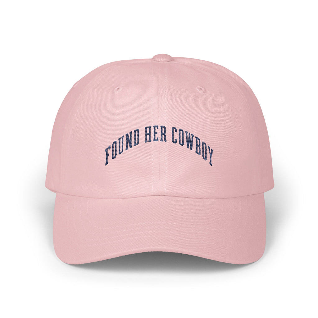 A pink baseball cap featuring the dark blue embroidered text Found Her Cowboy.