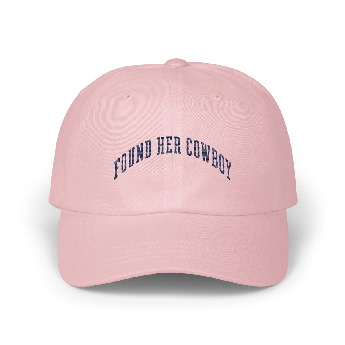 A pink baseball cap featuring the dark blue embroidered text Found Her Cowboy.