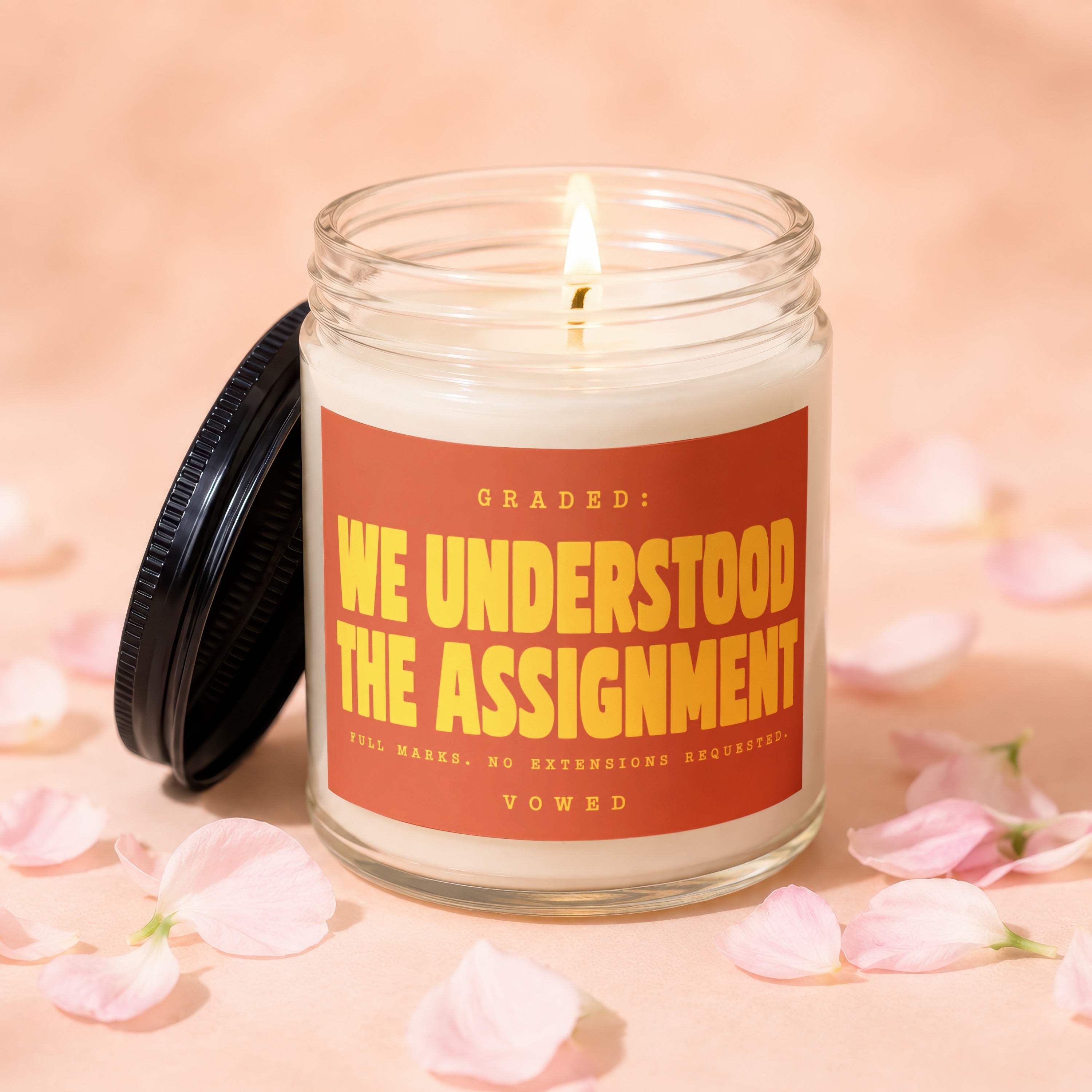 Candle with "We Understood The Assignment" text in yellow on orange label.