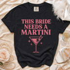 Black t-shirt with pink text "THIS BRIDE NEEDS A MARTINI" and a martini glass.